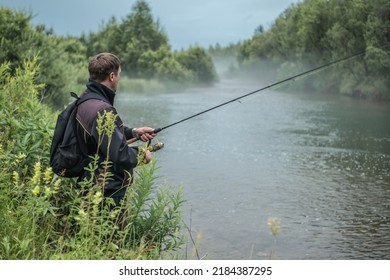Male fisherman is standing on the riverbank with a fishing rod in his hands and catching fish. Concept of Summer calm outdoor recreation, pastime, hobby - Shutterstock ID 2184387295