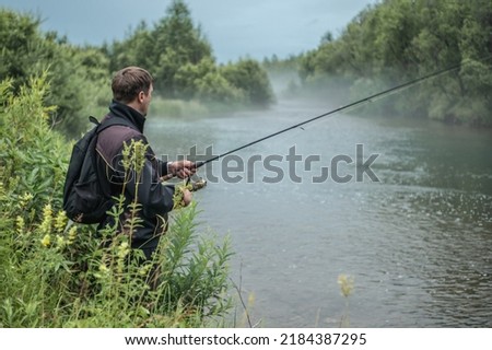 Male fisherman is standing on the riverbank with a fishing rod in his hands and catching fish. Concept of Summer calm outdoor recreation, pastime, hobby