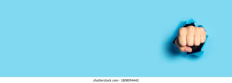 Male Fist Punches A Wall On A Blue Background. Banner. Breakout Gesture, Break