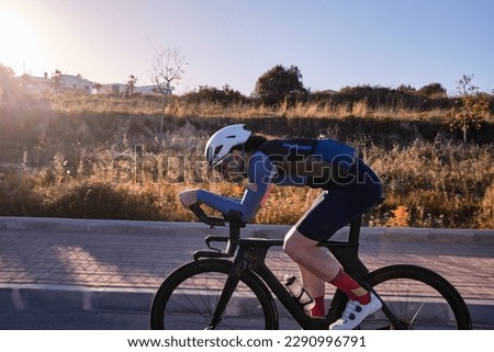 Male fit athlete riding time trial bicycle on empty road in golden hour. Sideview photo. Wearing helmet safety concept. Sport goal achieving. Extremely strong motivated person