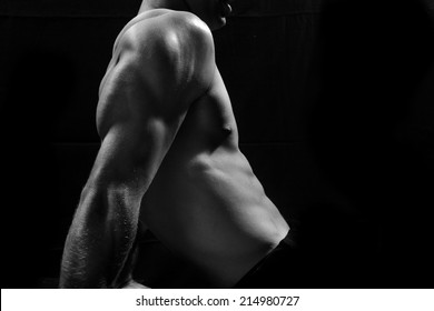 Male Fitness Model Showing Muscles In Studio With A Black Background