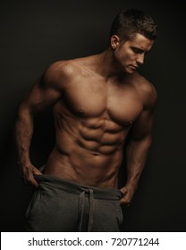 Male fitness model standing on black background with holding his pants