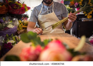 Male florist trimming flower stem at his flower shop - Powered by Shutterstock