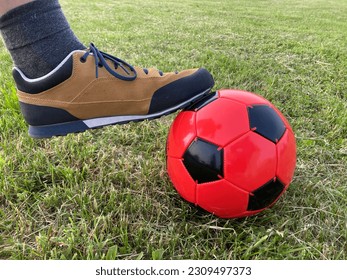 Male foot wearing sneakers on a football ball in a grassy field - Powered by Shutterstock