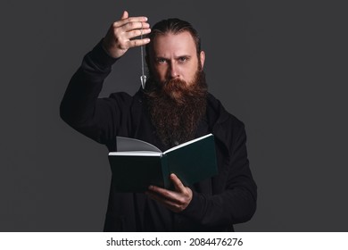 Male Fortune Teller With Book And Pendulum On Dark Background
