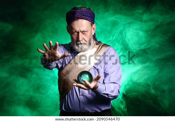 Male fortune teller with crystal ball on dark\
color background