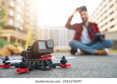 Male fpv pilot taking off goggles and checking his drone after landing on a street road. Operating multicopter experience, unmanned aviation concept. Focus is on the copter.