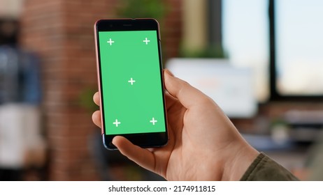 Male freelancer holding modern smartphone with greenscreen display, looking at blank mockup template. Working with isolated chroma key copyspace on mobile phone background in office. - Shutterstock ID 2174911815