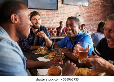 Male Friends Eating Out In Sports Bar With Screens In Behind