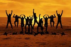 Male Friends Are Having Fun At Summer And Jumping Up On The Sunset Near The Sea Putting Their Hands Up To The Orange Sky