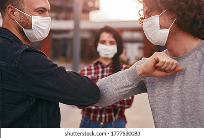 Male Friends In Masks Doing Elbow Bump While Greeting Each Other During Coronavirus Pandemic