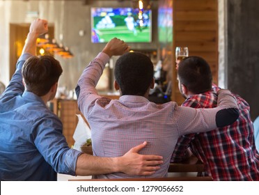 Male Friends Watching Football Match On TV In Sport Bar, Back View