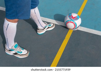 Male In Front Of A Soccer Ball Ready To Kick. Close Up Image Of A Person Getting Ready To Kick A White, Red, And Blue Ball In Front Of A Soccer Goal On A Blue Court With Yellow Lines.