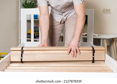 A male furniture assembler lays out wooden slats on a new white bed