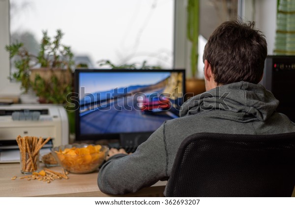 male gamer playing racing game on computer
with snacks lying on table - stock
photo