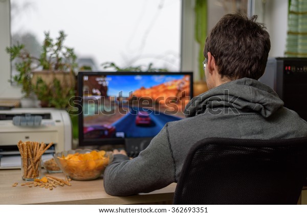 male gamer playing racing game on computer\
with snacks lying on table - stock\
photo