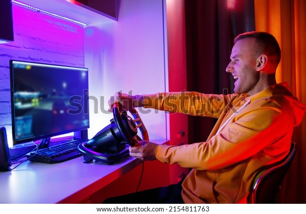Male gamer playing racing games on\
the computer. He uses the steering wheel. Emotional\
game