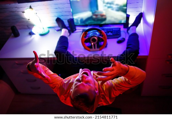 Male gamer playing racing games on\
the computer. He uses the steering wheel. Emotional\
game