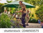 Male gardener raking the the flower bed while the collegue is sweeping the terrace in summer