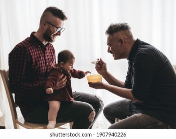 Male gay couple with adopted baby girl at home - Two handsome dads feed the baby girl on kitchen - Lgbt family at home, Diversity concept - Vintage filter