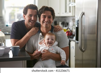 Male Gay Couple With Baby Girl In Kitchen Looking To Camera