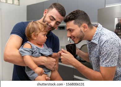 Male Gay Couple Holding Baby Girl In Their Kitchen