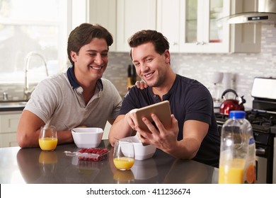 Male Gay Couple Looking At Tablet Computer Over Breakfast