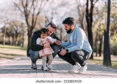 Male Gay Couple Playing With Their Daughter In The Park. Modern Family Concept.