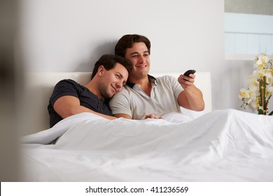 Male Gay Couple Relax In Bed Together Watching TV