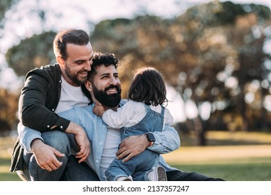 Male Gay Family Embracing And Happy In The Park With Their Little Daughter