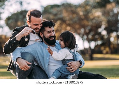 Male gay family hugging and playing with their little daughter in the park.