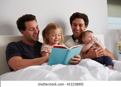 Male Gay Parents Reading A Book In Bed With Two Kids