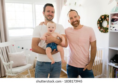 Male Gay Parents Relaxing In Baby Room Holding It