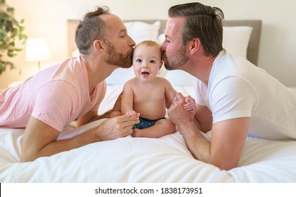 Male Gay Parents Relaxing In Bed With Baby