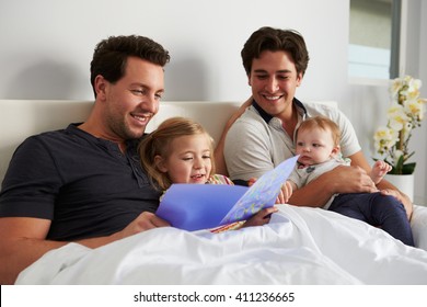 Male Gay Parents Relaxing In Bed With Two Kids