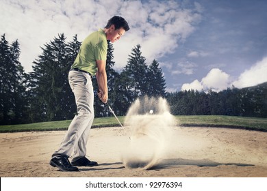 Male golf player in green shirt and grey pants hitting golf ball out of a sand trap with sand wedge and sand caught in motion. - Powered by Shutterstock