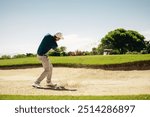 A male golfer expertly playing from a sand bunker on a lush golf course under a clear sky, highlighting dynamic game action.