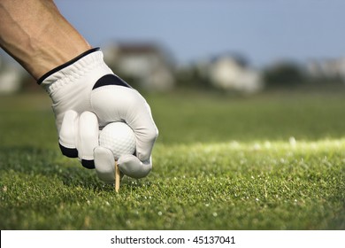 Male golfer places a golf ball and tee in the ground. Horizontal shot. - Powered by Shutterstock