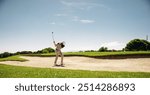 A male golfer skillfully swinging a golf club to escape a bunker during a competitive match, capturing determination and precision.