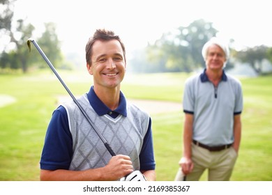 Male golfer smiling. Portrait of man holding a golf club and smiling with father in background.