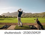 Male golfer taking a swing on a beautiful mountain course at a golf resort, his golf bag standing nearby. Perfect for golf enthusiasts and nature lovers.