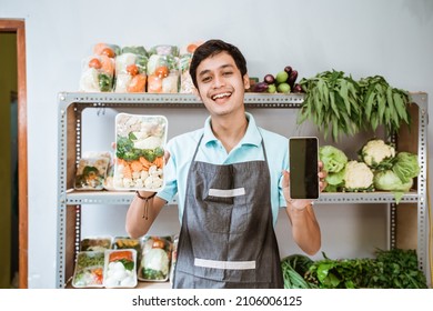 Male Greengrocer Showing Vegetables And Showing A Phone Screen