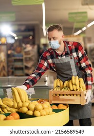 Male Grocery Store Worker Wearing Face Shield And Apron Standing In Store And Sorting Fruit. Handsome Caucasian Salesman In Mask Working Indoors. Supermarket Concept