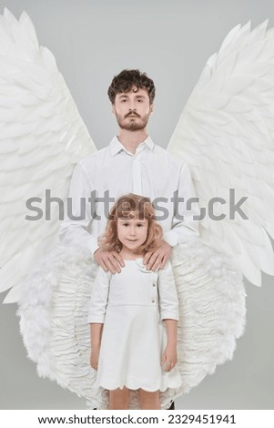 A male guardian angel and a small baby angel girl. White studio background. The concept of peace, hope and goodness.
