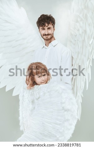A male guardian angel and a small baby angel girl. White studio background. The concept of peace, hope and goodness.
