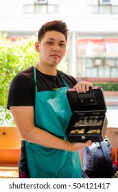 Male Guy Wearing A Green Apron Holding A Petty Cash Box Showing Its Coins