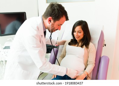 Male gynecologist using a stethoscope in the belly of a smiling pregnant woman and listening to the heartbeat of the baby 