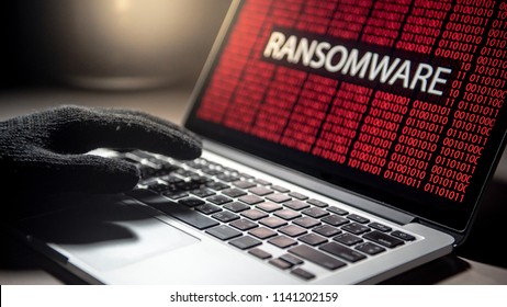 Male Hacker Hand On Laptop Computer Keyboard With Red Binary Screen Of Ransomware Attacking. Cyber Attack And Internet Data Security Concept