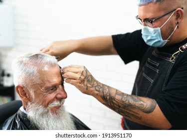 Male Hairdresser Cutting Hair To Beard Senior Client While Wearing Face Surgical Mask - Young Hairstylist Working In Barbershop During Corona Virus Outbreak - Health Care And Haircut Salon Concept