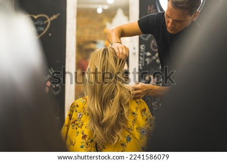 Male hairdresser focused on his job styling with comb his female client's blonde layered long hair in the professional hair salon. . High quality photo